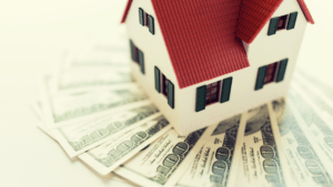 a toy house sitting on top of spread out hundred dollar bills